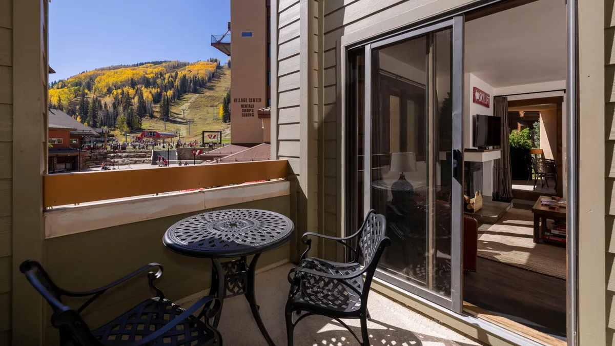 A small, private balcony featuring a round table and two chairs overlooking a beautiful mountain view. The scene is relaxed and intimate, suggesting morning coffee or stargazing moments.