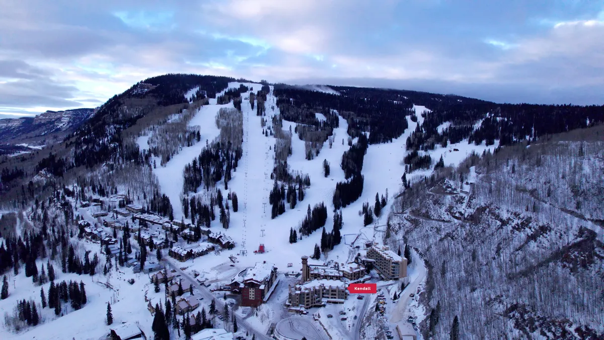 A sweeping view of the resort setting, with snow-dusted ski slopes in the background, cozy resort buildings nestled among pine trees, and the warm glow of sunset illuminating the San Juan Mountains. The image captures the inviting, adventurous spirit of the area.