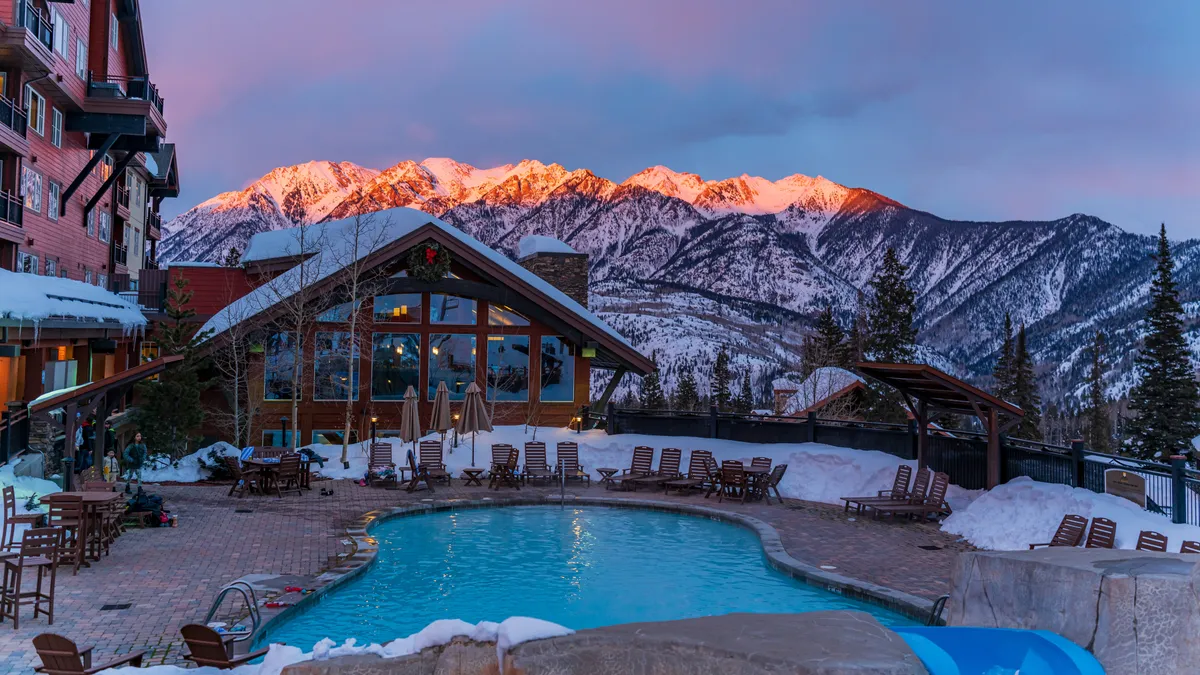 This exterior image showcases a sparkling swimming pool surrounded by lounge chairs, with a stunning mountain backdrop and the resort building featuring large windows. The scene is inviting, with an atmosphere of relaxation and leisure, ideal for families unwinding after a day of outdoor adventures.