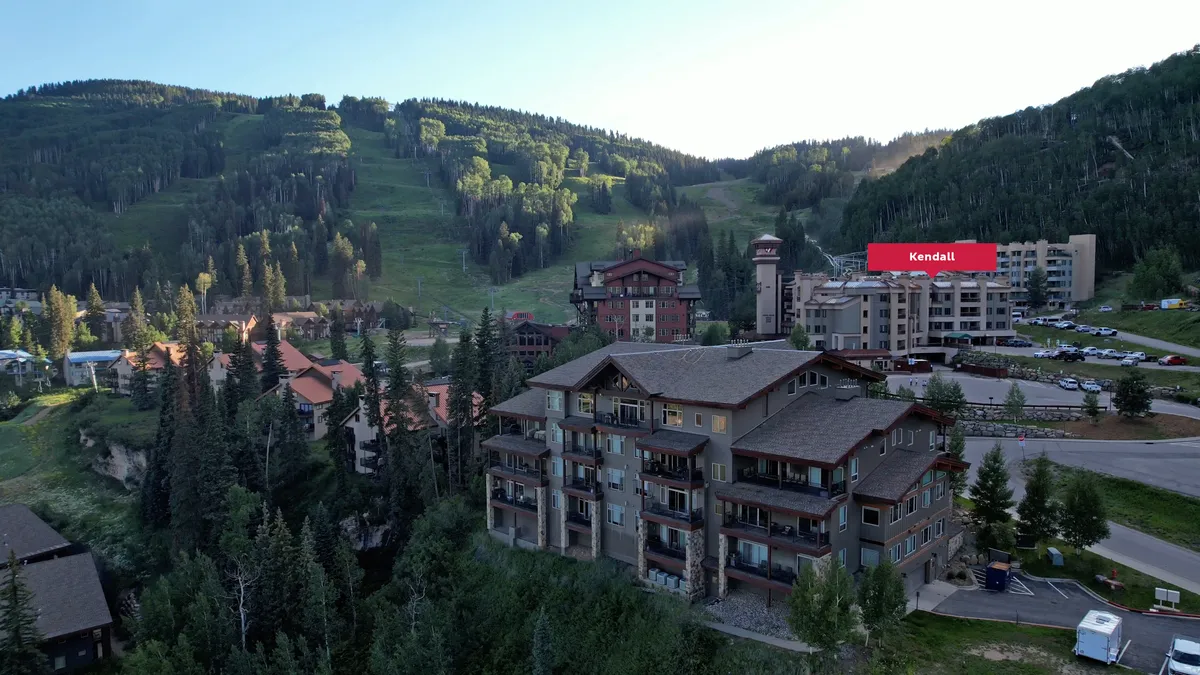 An exterior shot showing the resort’s residential buildings nestled in the mountains, with a visible parking area in the foreground. The landscape promises adventure with breathtaking views and hints at easy access and extra conveniences like parking and EV charging.