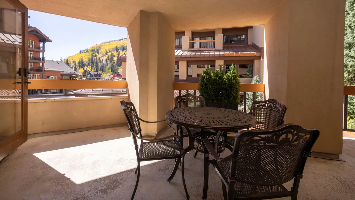 An outdoor dining setup on a balcony, with a table and chairs surrounded by lush greenery and a sweeping view of the mountains. The tranquil atmosphere is perfect for al fresco meals or relaxed morning coffees.